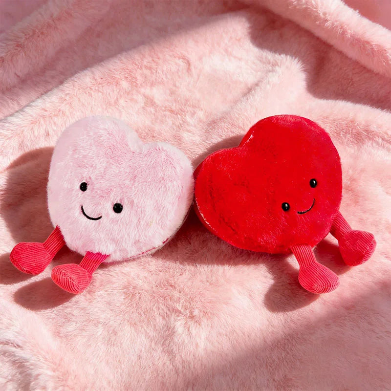 Two plush hearts, one pink and one red, resting on a fluffy pink background.