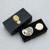 A black box containing a rose gold rhinestone pacifier and clip set with a gold charm.