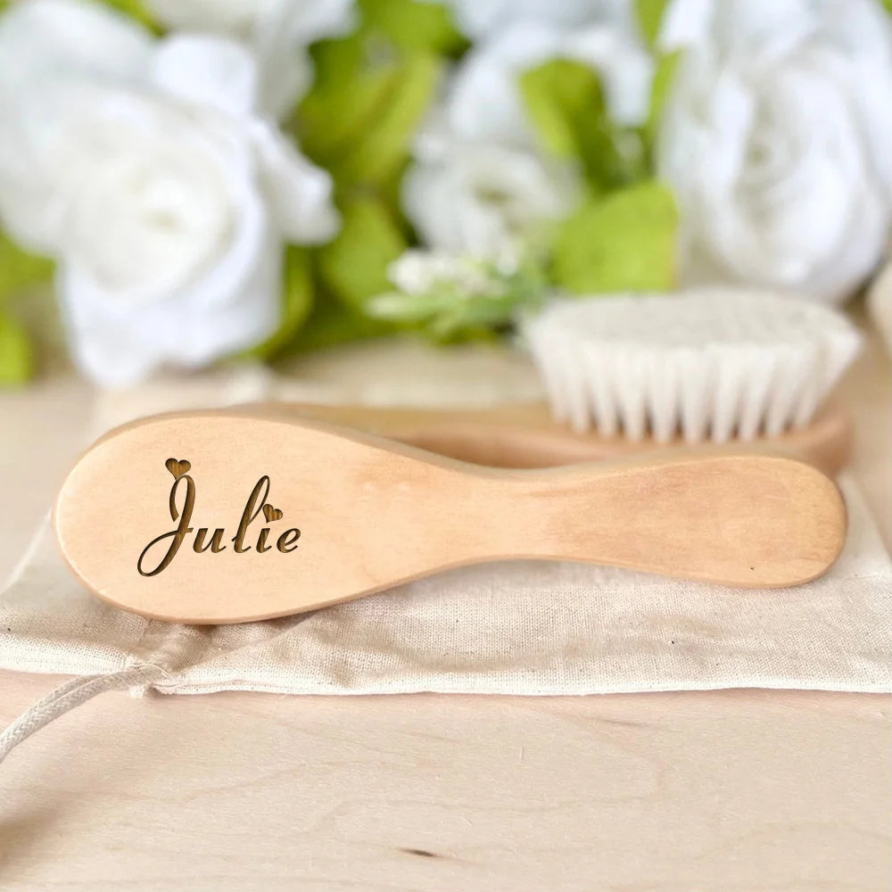 A light wooden baby brush and comb set with the name Julie engraved on the handle, resting on a beige cloth.