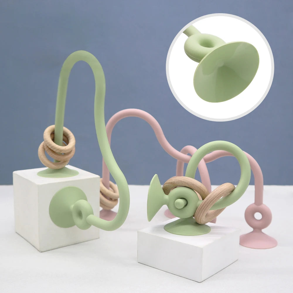 A set of soft silicone teether rings in pastel green and pink displayed on white blocks.