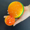 An orange squishy hamburger stress ball with green trim is held in a hand.