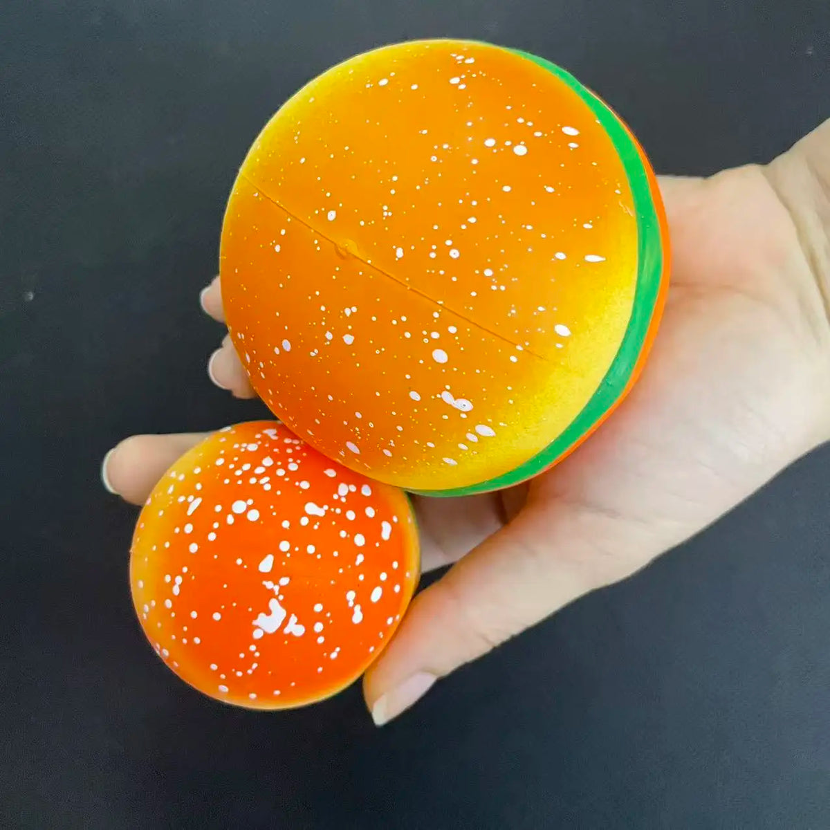An orange squishy hamburger stress ball with green trim is held in a hand.
