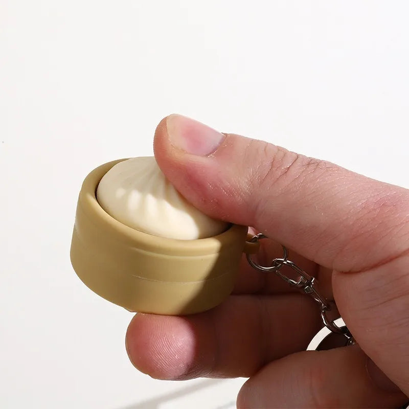 A hand holds a beige mini steamed bun fidget stress relief toy keychain.