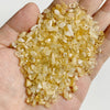 A hand holds a pile of yellowish-amber natural tumbled stone chips for jewelry making and home decor.