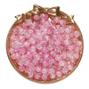 A circular display of pink glass crackle beads arranged in a mound, tied with a gold bow.