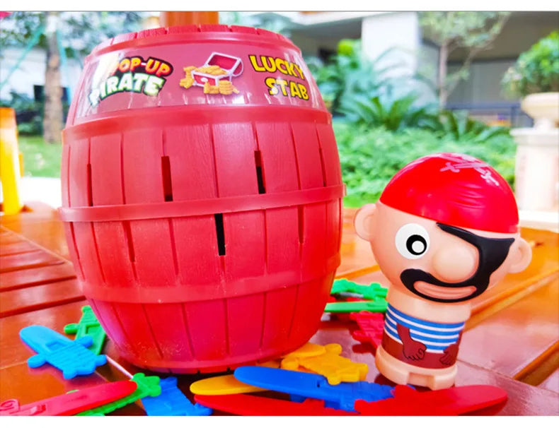 A red pirate barrel game with a sword stab piece and a small plastic pirate figure on a wooden surface.