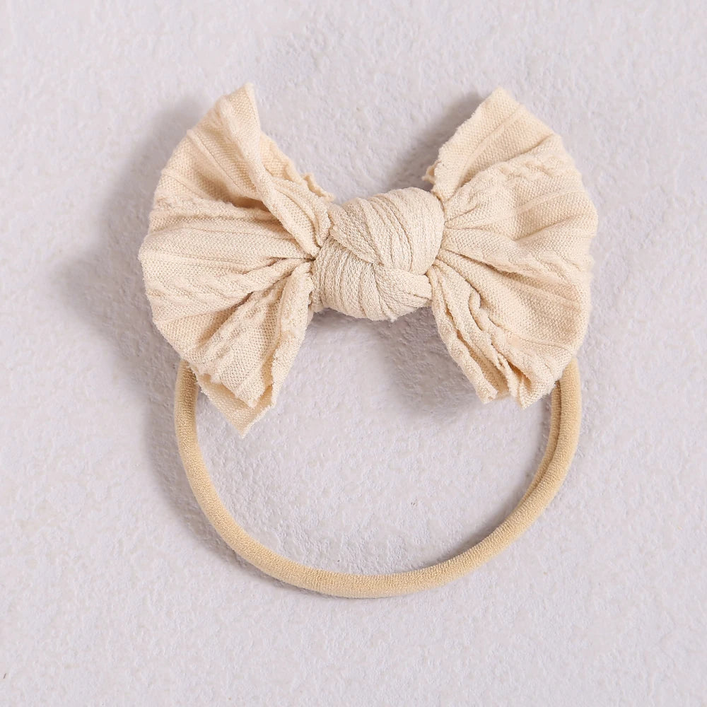 A beige knitted fabric bow headband with a soft elastic band.