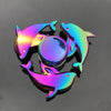 A rainbow metal fidget spinner featuring three stylized fish shapes and a central sphere rotating on a dark surface.