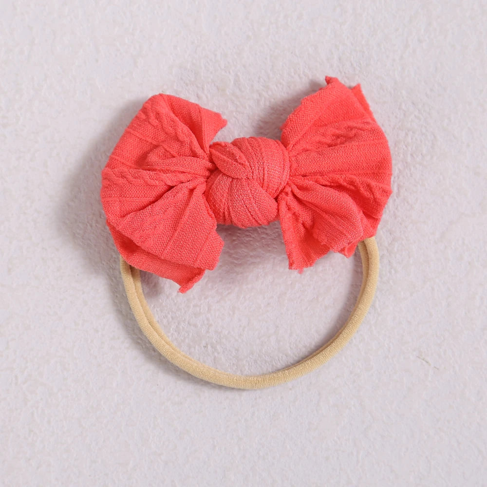 A bright coral pink fabric bow headband with a soft elastic band.
