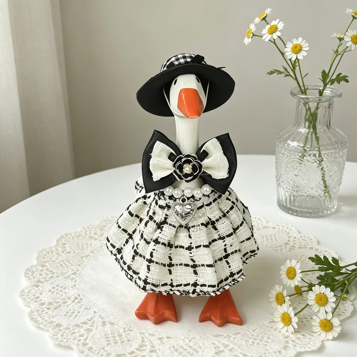 A handcrafted mini goose statue dressed in a black and white plaid outfit with a bow and floral accessories.