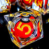 A close-up of a red resin die with the number 5 and gold accents, set against a dark reflective surface.