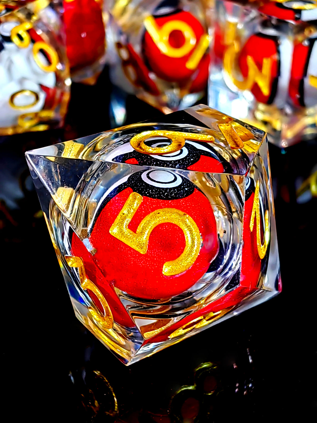 A close-up of a red resin die with the number 5 and gold accents, set against a dark reflective surface.