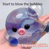A hand holds a purple and blue octopus bubble stress ball with a pink nose.