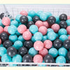 A white basket filled with a 50-pack of colorful play balls in shades of pink, blue, and black.
