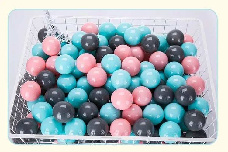 A white basket filled with a 50-pack of colorful play balls in shades of pink, blue, and black.
