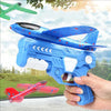 A hand holds a blue foam glider catapult toy gun with a blue and red patterned glider attached, set against a blurred outdoor