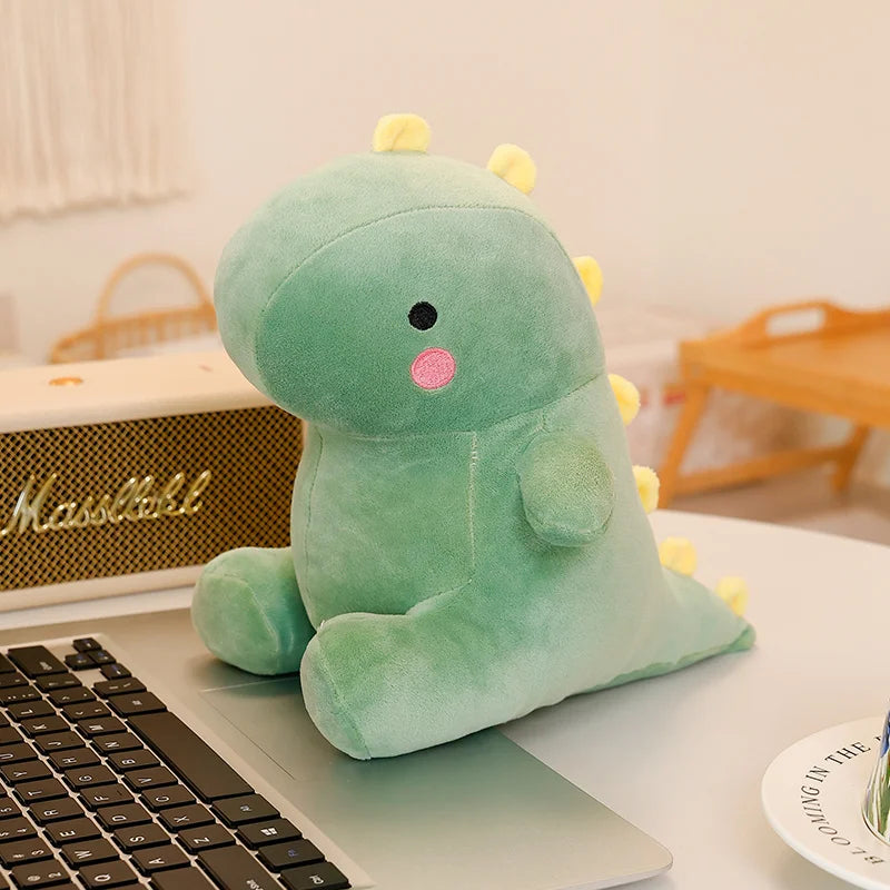 A soft, light green dinosaur plush toy resting on a laptop keyboard.