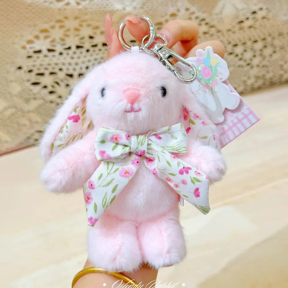 A pink soft bunny plush toy with a bow charm keychain is held by a hand.