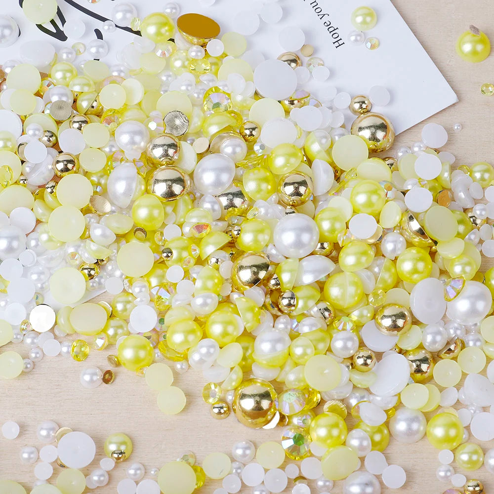 A pile of mixed resin rhinestone pearls in yellow and white with gold accents for crafts and nail art