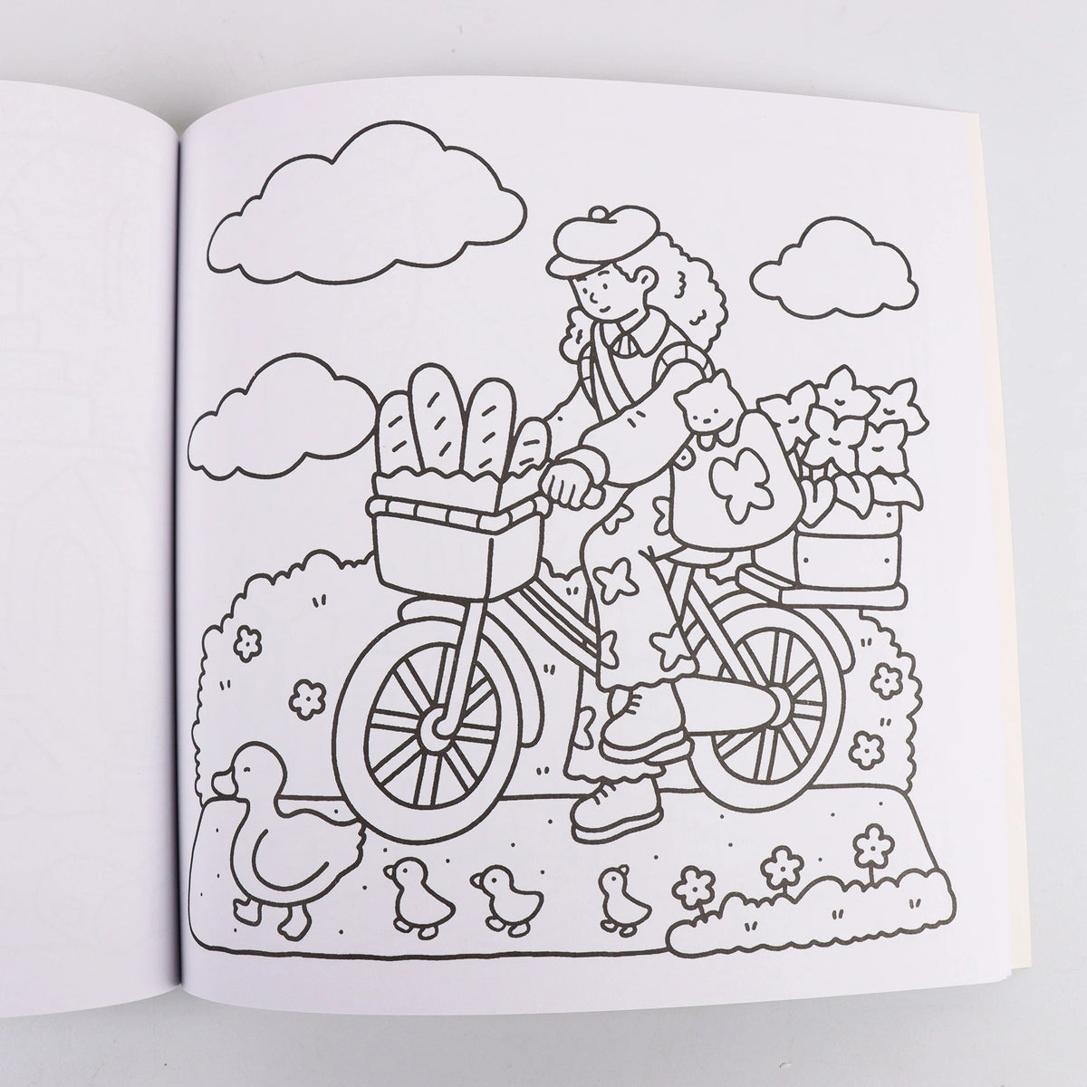 A black and white line drawing of a woman riding a bicycle loaded with bread and flowers through a grassy field under a cloud