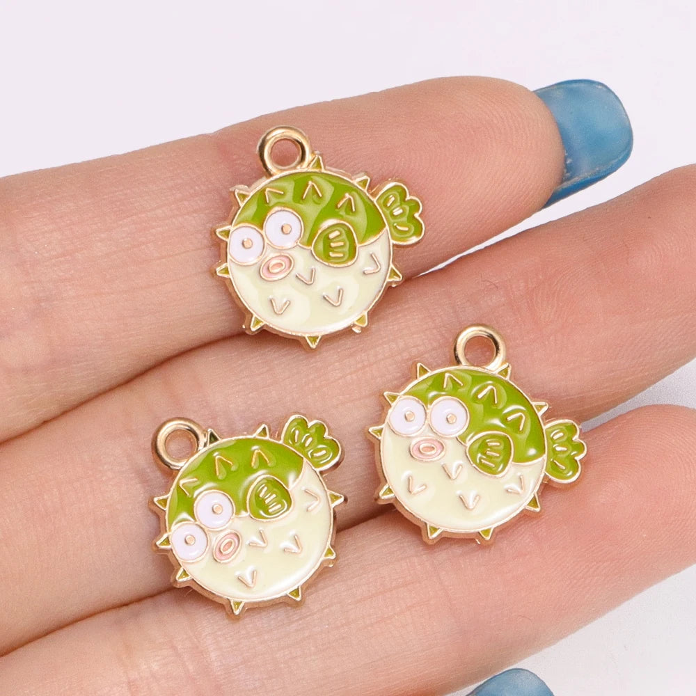 A hand holds three enamel marine life charms shaped like green sea turtles with pink accents.
