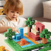 A young child is building a model using green and blue magnetic building cubes on a green mat.