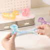 A hand holds a clear, sparkly blue dachshund squishy toy next to pink and yellow plush toys.