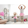 A young girl wearing a pink tutu dress and light gray pants poses with her arms raised in a celebratory gesture.