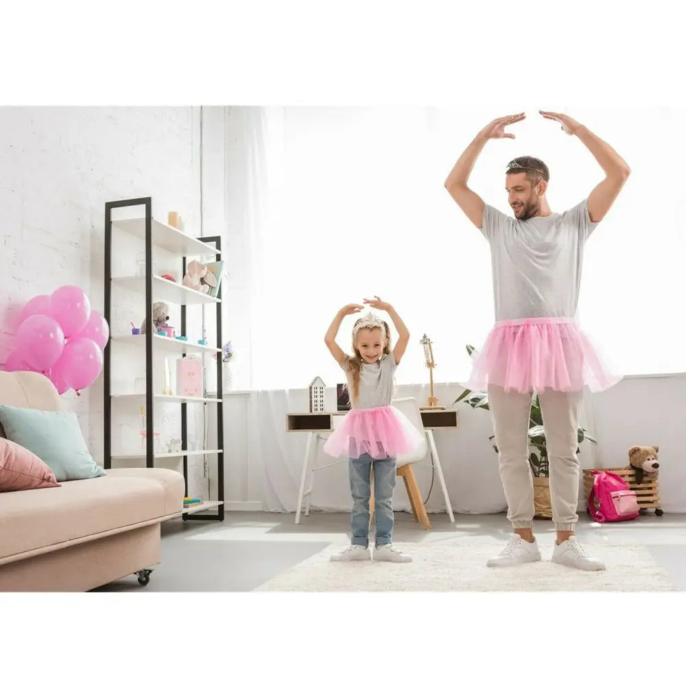 A young girl wearing a pink tutu dress and light gray pants poses with her arms raised in a celebratory gesture.