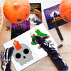 A Halloween coloring book set featuring festive pages, a pumpkin, and a skeleton design on a wooden surface.