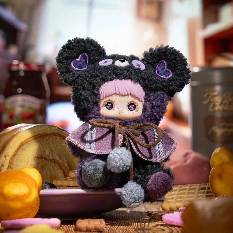 A dark purple and black bear plush charm with pink accents sits on a wooden surface surrounded by various food items.