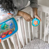 A hand is placing an orange star-shaped toy into the clear viewing window of an ocean-themed crib soother.