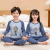 A boy and a girl wearing matching blue cotton pajama sets with an astronaut theme sitting on a bed.