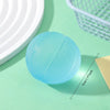 A light blue, textured squishy fidget toy is shown on a green surface next to a white plate and a green mesh basket.