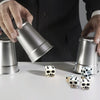 A hand is holding a silver tin while white skull dice are displayed on a white surface.