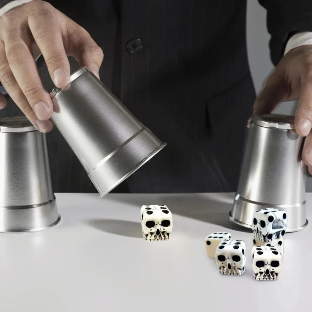 A hand is holding a silver tin while white skull dice are displayed on a white surface.