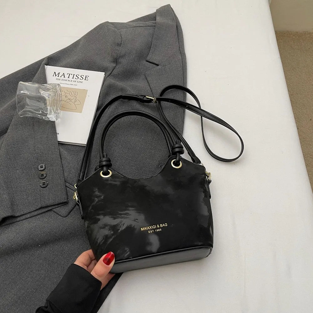 A black floral canvas tote bag with a leather strap is displayed next to a gray blazer and a magazine.