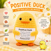 A handmade yellow crochet duck doll with a motivational message card sitting on a wooden surface.