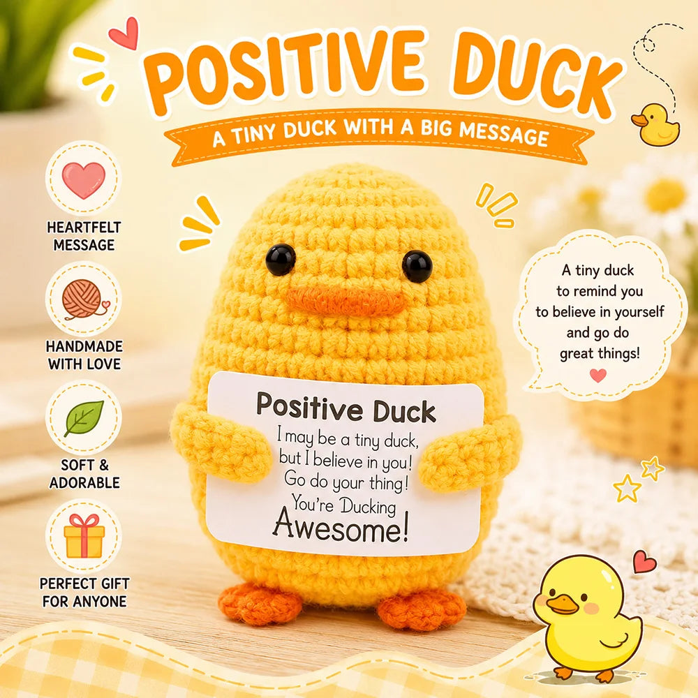 A handmade yellow crochet duck doll with a motivational message card sitting on a wooden surface.