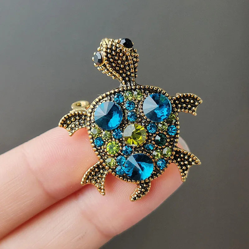 A gold-toned rhinestone turtle brooch pin featuring various blue and green gemstones.