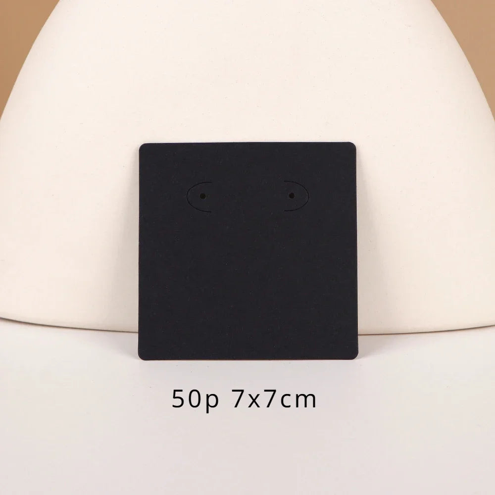 A black square jewelry display card with two small eyes is shown against a light background.
