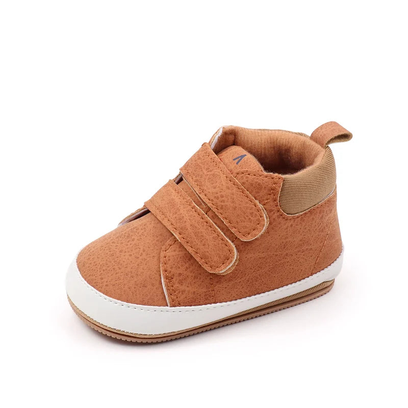 A pair of brown soft PU leather baby first walker shoes with a white anti-slip sole.