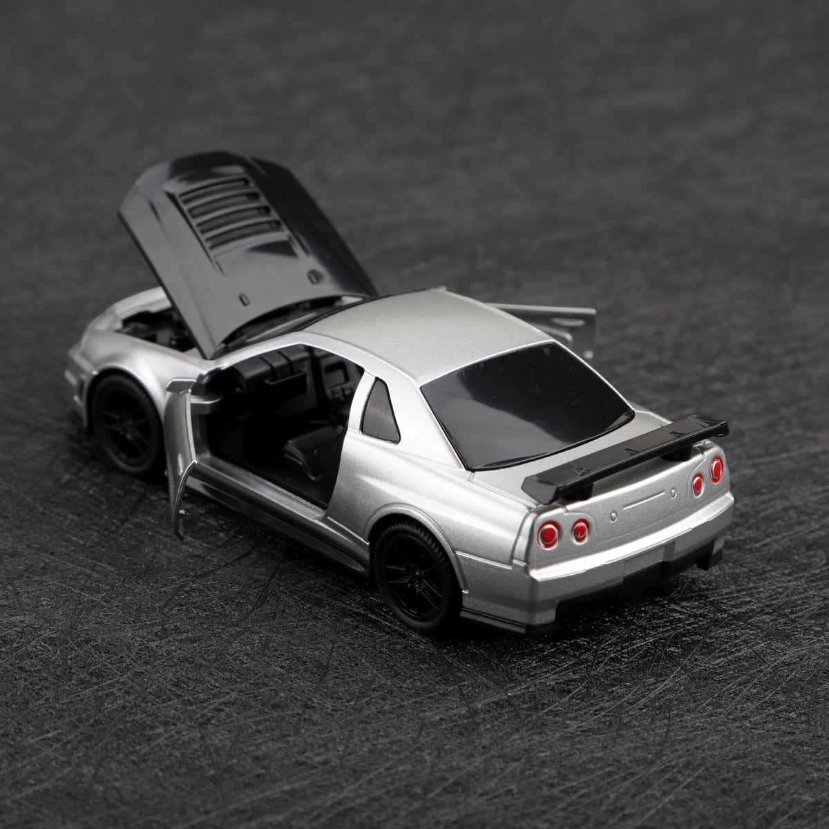 A silver die-cast sports car with a hood open is shown on a dark surface.