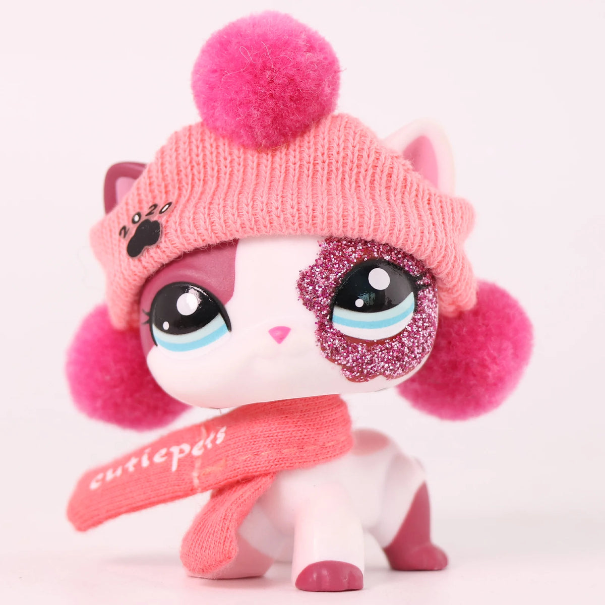 A pink and white cat bobble head figurine wearing a pink knitted hat and a sparkly face paint.