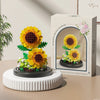 A box of DIY micro building blocks featuring a yellow flower and pink blossoms, displayed on a white stand.