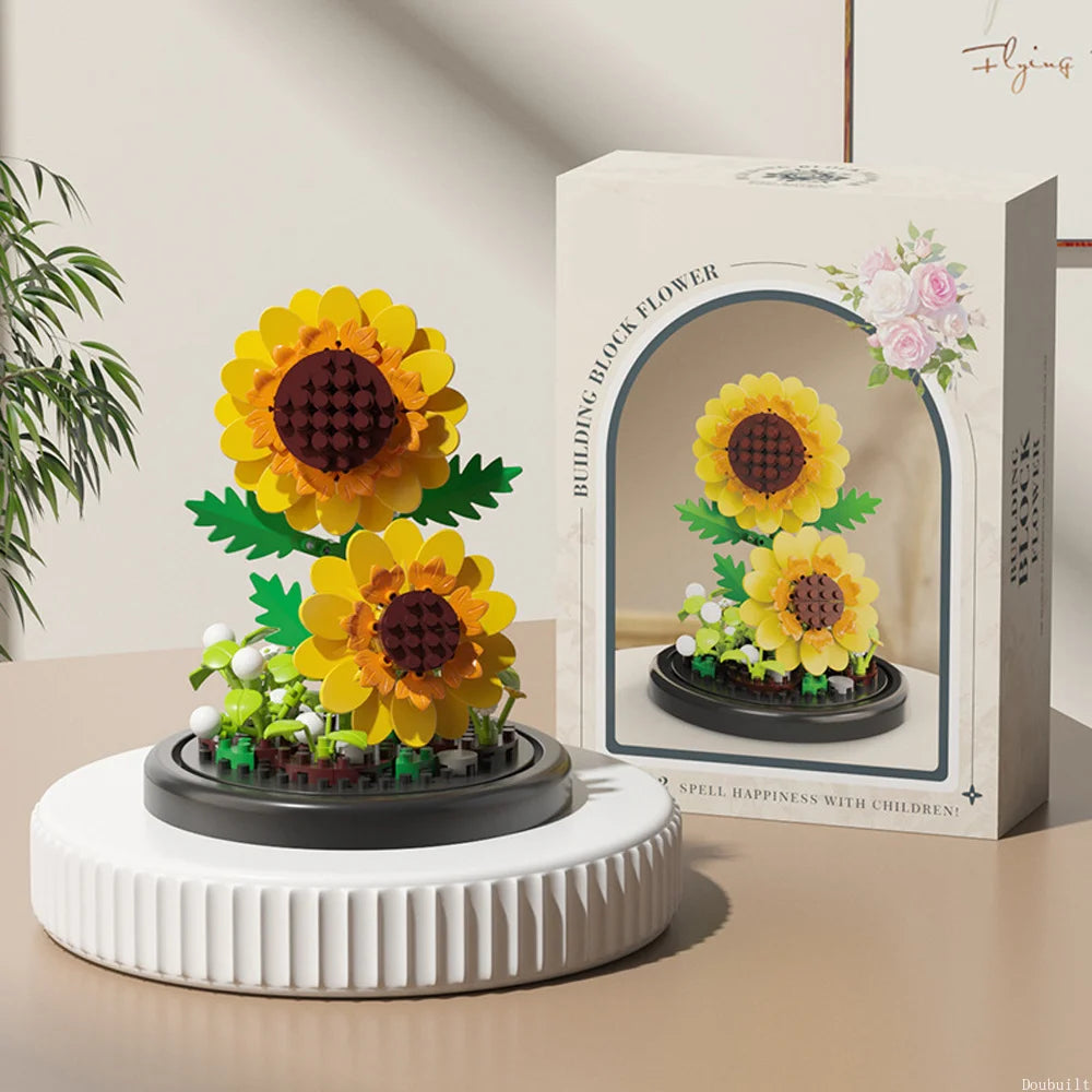 A box of DIY micro building blocks featuring a yellow flower and pink blossoms, displayed on a white stand.