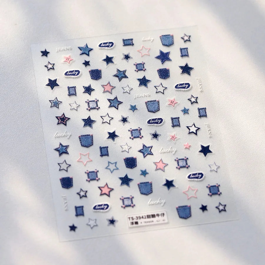 A sheet of nail art stickers featuring various star and geometric shapes in blue, pink, and gray tones.