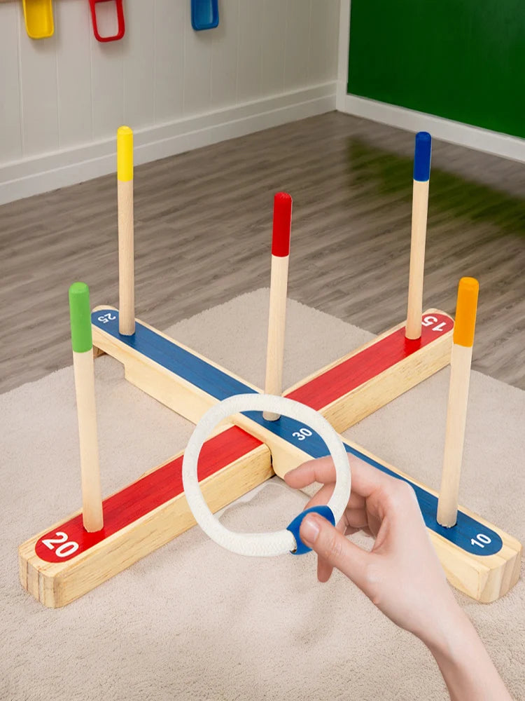 A hand is holding a white ring on a wooden ring toss game with colored wooden pegs and numbers.
