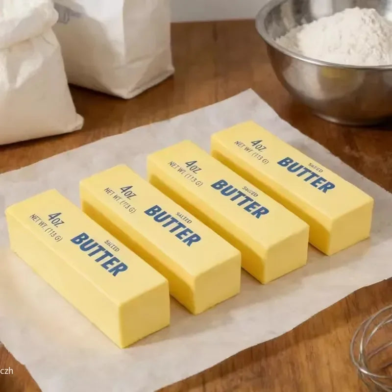 Yellow butter sticks labeled 4oz each are arranged on parchment paper next to a bowl of butter