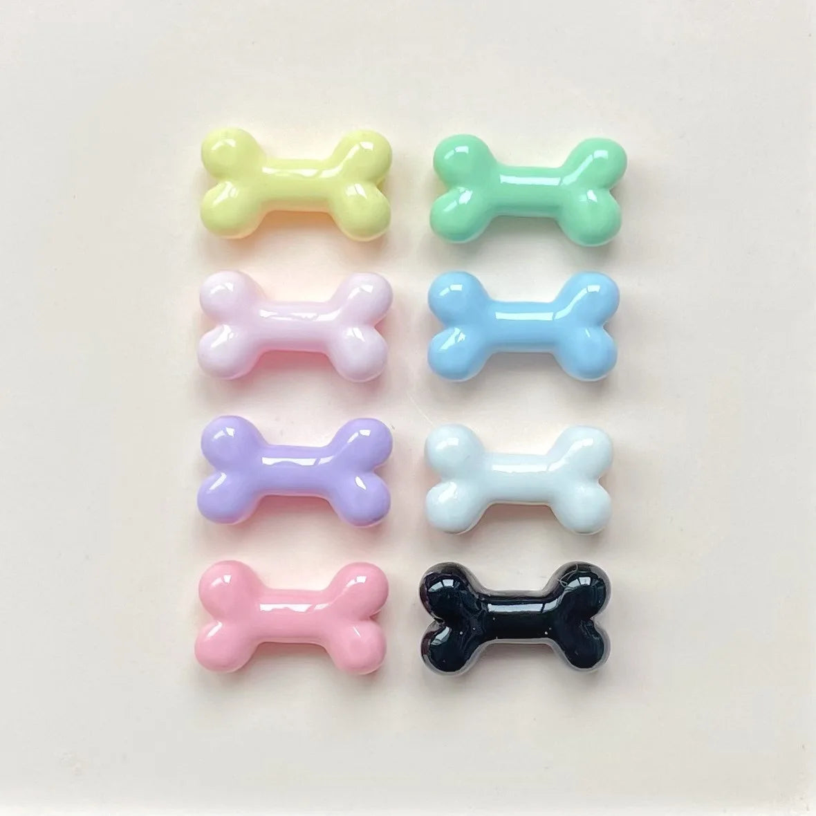 A collection of six small, bone-shaped resin charms in various pastel colors including yellow, green, pink, blue, purple, and